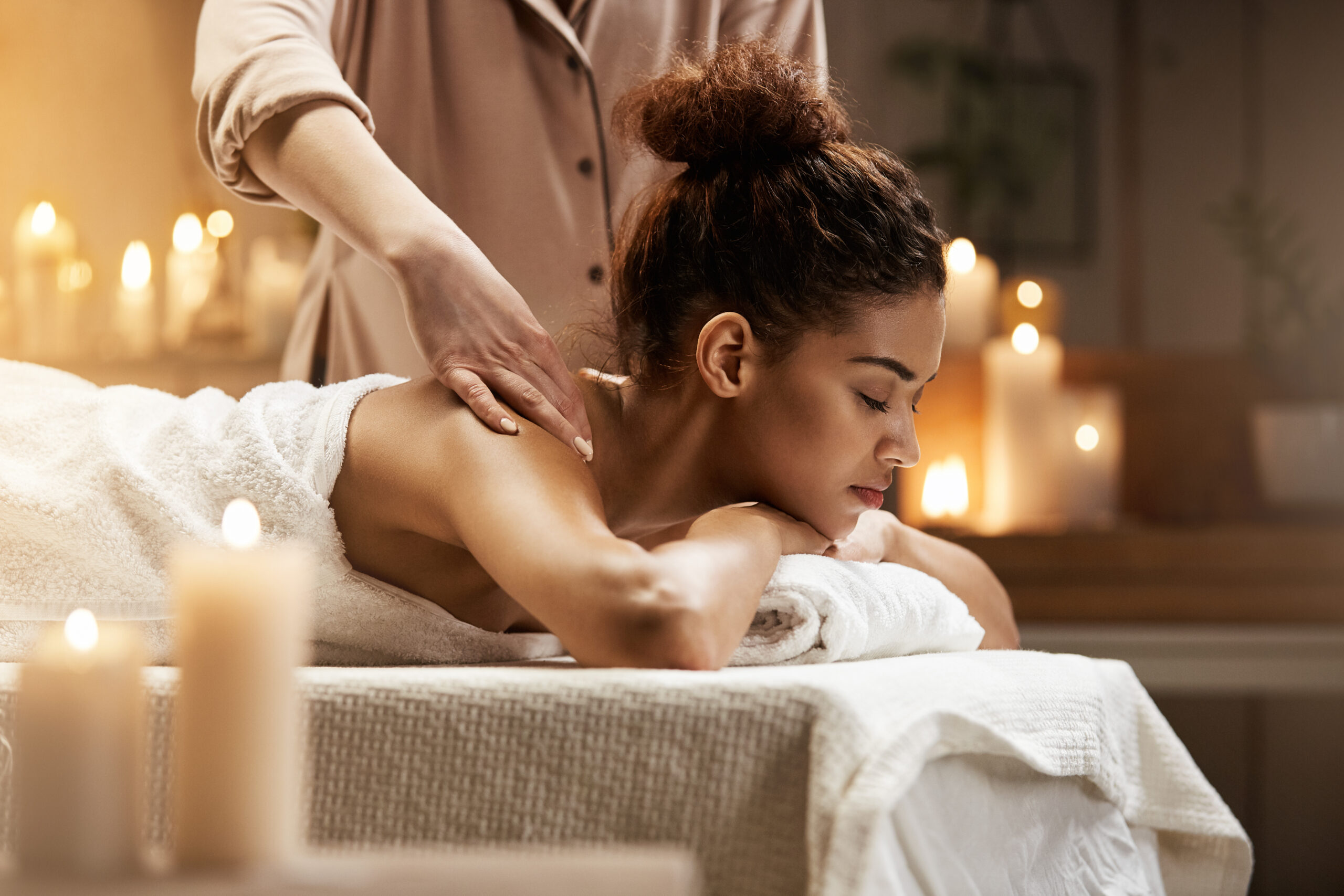 Young tender african girl smiling enjoying massage with closed eyes in spa resort.
